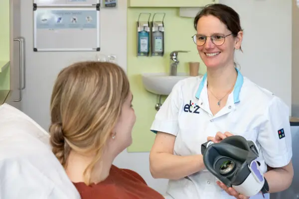 Een zorgmedewerker houdt een VR-bril vast en biedt deze aan bij een patiënt