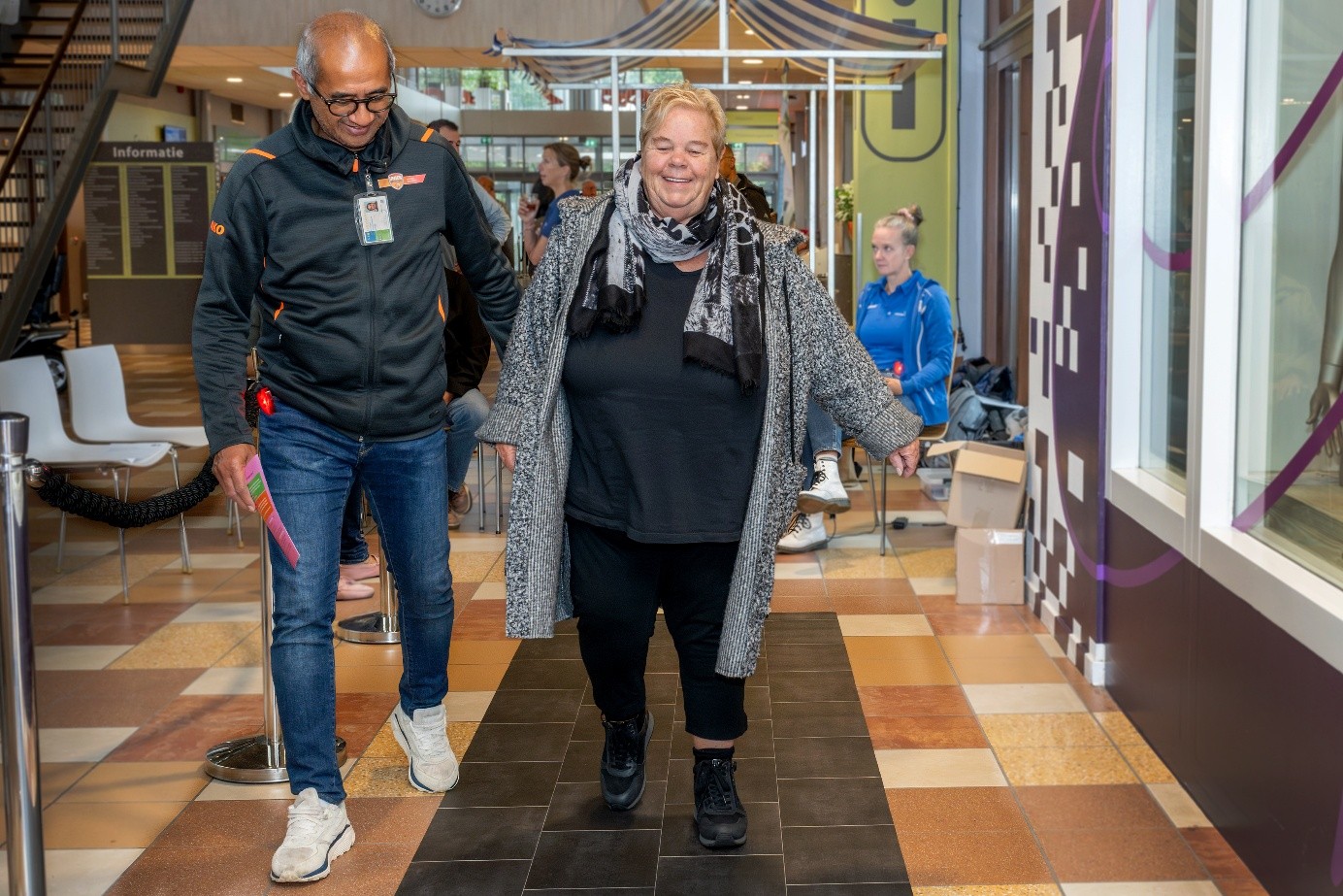 Een vrouw loopt over een testmat in de hal van het ETZ. De mat bestaat uit veel verschillende vlakken. Ze wordt begeleid door een expert